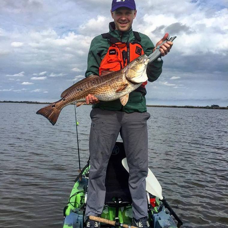 a man standing in a kayak holding a large fish
