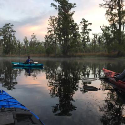three kayakers paddling away at sunset