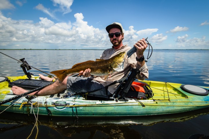 A wide shot of a man showing off a fish in a kayak